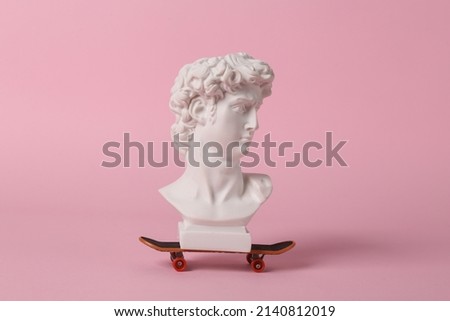 David bust with skateboard on pink background. Minimal contemporary still life
