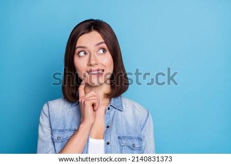 Photo of thoughtful pretty lady dressed denim shirt biting lip looking empty space isolated blue color background