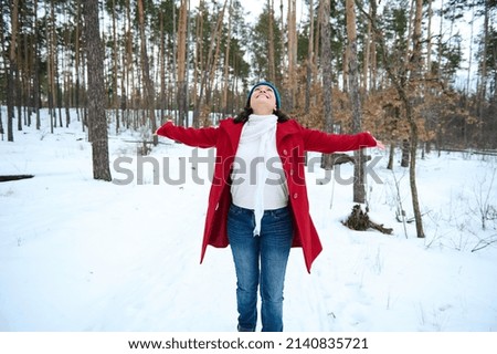 Happy cheerful woman raising arms up while whirling in a snow covered nature, enjoying beautiful cold winter day while walking on a snowy pine forest. Wonderful winter, cool weather Royalty-Free Stock Photo #2140835721