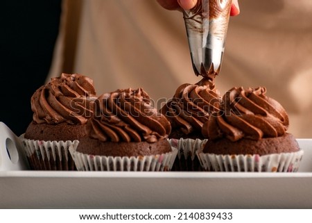 Pastry chef decorates cupcakes with chocolate cream from pastry bag. Homemade cocoa muffins close up Royalty-Free Stock Photo #2140839433