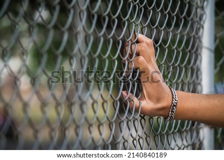 The young man's hand clinging to the lattice fence outside the building due to imprisonment. The idea of imprisoning prisoners of war to prevent escaping and to negotiate with the enemy. Royalty-Free Stock Photo #2140840189