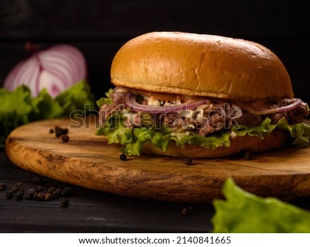 burger with minced beef, red onion and lettuce leaf on a wooden board and dark wooden background
