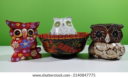 3 owls in one picture. one is made of porcelain and stands in an ornate wooden bowl. 2 more made of wood with colorful decorations are on her left and right