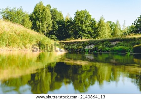 Calm summer landscape with tranquil river water and reflection of forest trees in it