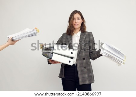 Stressed female worker and business woman holding a pile of paperwork while getting more work to do. Looking frustrated in camera, isolated on white background. Concept: Too much work Royalty-Free Stock Photo #2140866997