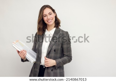 Beautiful and smiling business woman with paperwork in hands, standing isolated on white, looking happy about the papers she's holding and smiling in to the camera.
