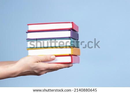 Female hands holding pile of books over light blue background. Education, self-learning, book swap, hobby, relax time