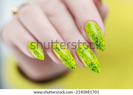 Female hand with long nails and a bottle of bright yellow green neon nail polish