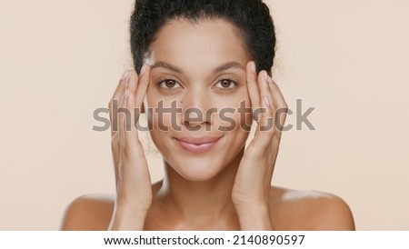 Close-up beauty portrait of young African American woman who lifts her eyes touching her face on beige background | Droopy eyes removal concept Royalty-Free Stock Photo #2140890597