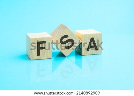 FSA - an abbreviation of wooden blocks with letters on a blue background. Reflection of the caption on the mirrored surface of the table. Selective focus. fsa - shortt for flexible spending account