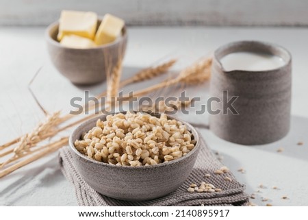 Bowl of cooked peeled barley grains porridge with ears of wheat on white background. Cooking Healthy and diet food concept. Royalty-Free Stock Photo #2140895917