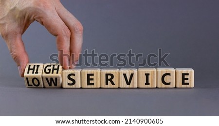 Low or high service symbol. Businessman turns cubes and changes words low service to high service. Beautiful grey table grey background. Business low or high service concept, copy space.