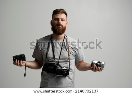 Portraite of professional handsome bearded male photographer with bunch of vintage photo cameras in photo studio, isolated on white background.