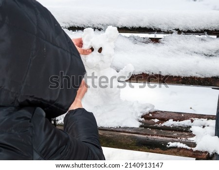 Girl makes snowman outdoors in snowy winter park. Seasonal fun activities. He puts stones in his little snowman's eyes.
