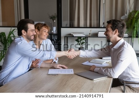Confident lawyer meeting and shaking hands with happy couple of clients. Husband and wife visiting office of mortgage broker, real estate agent, house seller shaking hands over signed contract Royalty-Free Stock Photo #2140914791