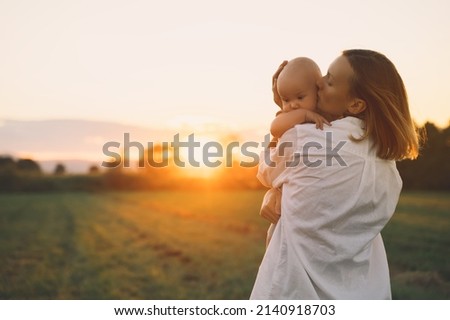 Loving mother and baby at sunset. Beautiful woman and small child in nature background. Concept of natural motherhood. Happy healthy family at summer outdoors. Positive human emotions and feelings. Royalty-Free Stock Photo #2140918703