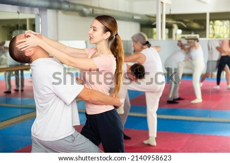 Determined young woman attacking eyes of male sparring partner as self-defense tactic during workout in practice hall