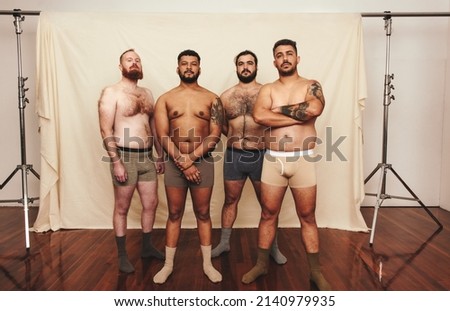 Young men standing shirtless against a studio background. Group of body positive young men wearing underwear in a modern studio. Self-confident young men embracing their natural bodies.