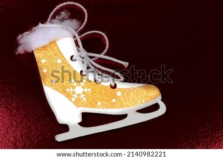 Antique gold toy skates made of wood on a dark red background.