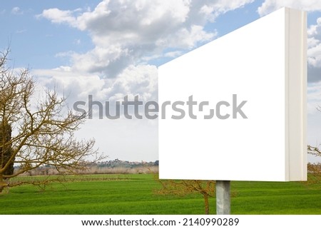 Blank advertising signboard in a green field with trees on background in a Tuscany landscape (Italy) - concept with copy space for text inserting 