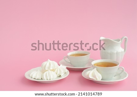 Tea and marshmallows. Black tea with lemon in white porcelain cups, porcelain milk jug and sweets on a pink background