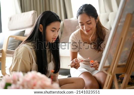A pretty young girl learning acrylic painting on canvas easel with her private art teacher in her house. Painting concept.