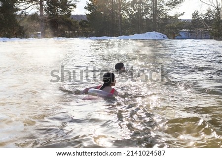 a girl in a circle swims in salt water in winter, clouds of steam rise above hot water in a salt spring of healing, nature in contrast