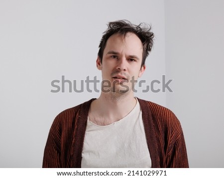 young caucasian man standing against a white isolated background. emotions of depression, anger, and frustration. A man in a cardigan with messy, disheveled hair. 
Portrait of one sad man  Royalty-Free Stock Photo #2141029971