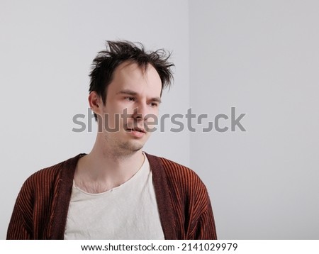 young caucasian man standing against a white isolated background. emotions of depression, anger, and frustration. A man in a cardigan with messy, disheveled hair. 
Portrait of one sad man  Royalty-Free Stock Photo #2141029979