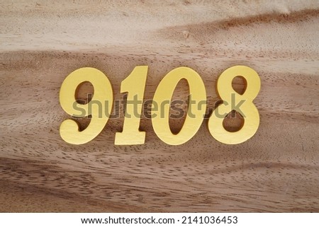 Wooden  numerals 9108 painted in gold on a dark brown and white patterned plank background.