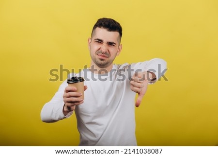Smiling young man in white jacket posing isolated on yellow orange background, studio portrait. People lifestyle concept sincere emotions. Layout copy space. Holding coffee in his hands
