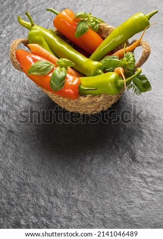 Traditional basket with fresh seasonal vegetables: green pepper, tomato, onion, carrot, cucumber, basil, dill on gray black background, top view, stock photo