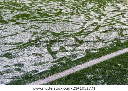 The football field with artificial green grass is covered with a light layer of snow. Early spring. Green grass on the football field is visible from under the snow. Amateur football field.