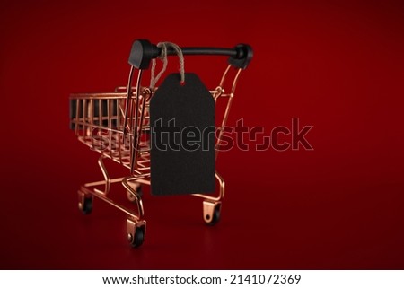 Black sale tag and golden shopping cart over red background with copy space for text. Black Friday sale, shopping concept