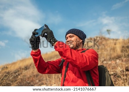 Man traveler using smart phone mobile phone to take pictures on adventure trip at holidays. Use smartphone selfie on rocky mountains at vacations outdoor. Travel lifestyle concept.