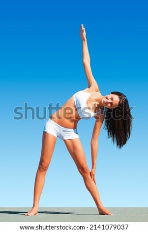 Feeling the stretch. A fit young woman doing yoga while against a blue sky (Trikonosana).
