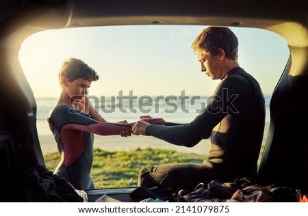 Thats what big brothers are for. Shot of a young surfer helping his little brother put on his wetsuit at the beach. Royalty-Free Stock Photo #2141079875