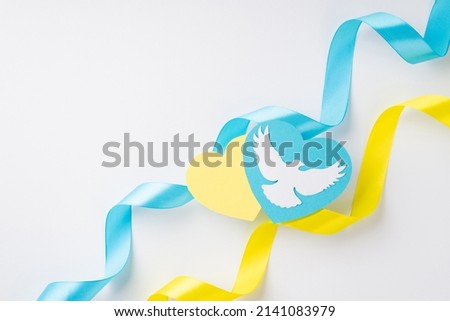 Stop the war in Ukraine concept. Top view photo of national flag colors yellow and blue curly ribbons and hearts with white pigeon on isolated white background