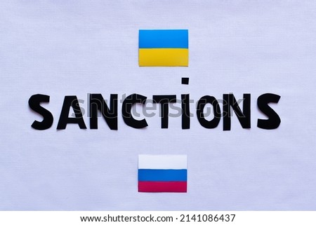 Top view of sanctions lettering near ukrainian and russian flags on white background