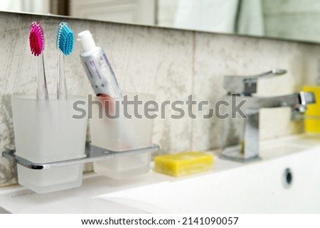 glass with two colored toothbrushes and soap in  bright defocused bathroom with  mirror.