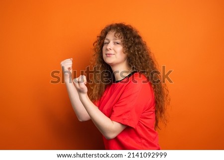 Picture of pretty redhead female fan in sport football uniform keeping fists for her football team victory, human emotions concept.