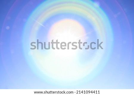 Iridescent circular glare from the bright sun on the blue sky. Beautiful background to illustrate celestial phenomena, aura, high vibrations, the universe  Royalty-Free Stock Photo #2141094411