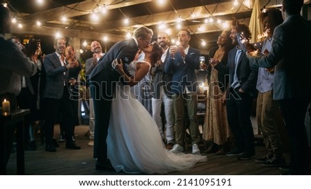 Beautiful Bride in White Dress and Groom in Stylish Black Suit Celebrate Wedding at an Evening Reception Party. Newlyweds Dancing at a Venue with Best Multiethnic Diverse Friends. Royalty-Free Stock Photo #2141095191