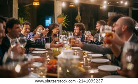 Big Dinner Party with a Small Crowd of Multiethnic Diverse Friends Celebrating at a Restaurant. Beautiful Happy Hosts Propose a Toast and Raise Wine Glasses while Sitting at a Table in the Evening. Royalty-Free Stock Photo #2141095237