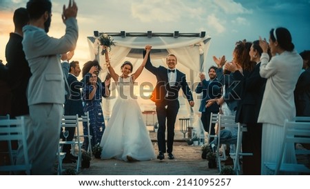 Beautiful Bride and Groom Celebrate Wedding Outdoors on a Beach Near the Ocean at Sunset. Perfect Marriage Venue with Best Multiethnic Diverse Friends Throwing Flower Petals on the Newlyweds. Royalty-Free Stock Photo #2141095257