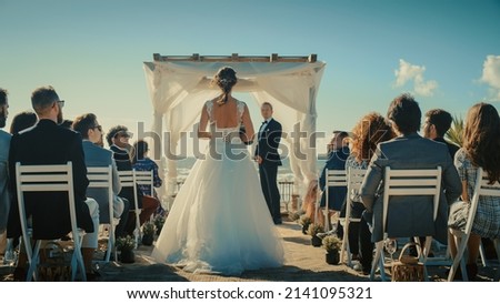 Beautiful Bride in Gorgeous White Wedding Dress Going Down the Aisle, while Groom Waits at an Outdoors Ceremony Venue Near the Sea with Happy Multiethnic and Diverse Friends. Royalty-Free Stock Photo #2141095321