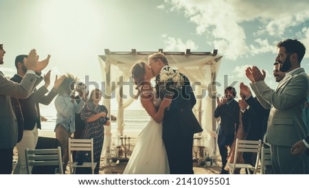 Beautiful Bride and Groom Celebrate Wedding Outdoors on a Beach Near the Ocean. Perfect Marriage Venue with Best Multiethnic Diverse Friends Throwing Flower Petals on the Newlyweds. Royalty-Free Stock Photo #2141095501