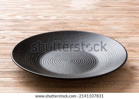 Perspective view of empty black plate on wooden background. Empty space for your design. Royalty-Free Stock Photo #2141107831