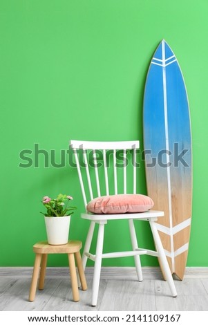 Stool with houseplant, chair and surfboard near color wall in room