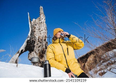 A tourist man drinks tea from a mug, breakfast in nature in sunny weather, a spring hike through the forest, a young traveler on a winter hike, a thermos with hot tea. High quality photo